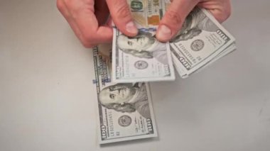 Beyaz bir masada eski 100 dolarlık banknotları saymak. Erkek eller kağıt para sayıyor, ev parası. 100 dolarlık banknotlar sayan bir elin yakın çekimi. İş, finans, ekonomi kavramı.