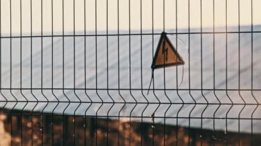 Güneş santralinin tel örgüsünde yüksek voltaj işareti var. Sarı üçgen şimşek işareti yüksek voltaj tehlikesi. Elektrik santralinin elektrik güvenlik sembolü uyarısı. Elektrik şoku tehlikesinin işareti.