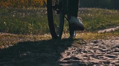 Güneşli bir yaz gününde yeşil orman yolunda bisiklet süren genç bir kadın. Ağır çekim. Bisikletli bir kadın kırsalda yeşil çimlerin çok yakınında patikaya çıkıyor. Sağlıklı bisiklet yaşam tarzı, boş zaman aktivitesi.