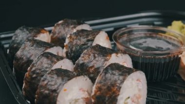 Japon suşi ruloları plastik kutuda dönüyor, yakın plan. Zencefilli, wasabi ve soya soslu taze suşi. Philadelphia peynirli suşi, nori, yengeç çubuğu, somon filetosu ve salatalık..