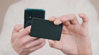 Akıllı telefonu olan genç bir adam soğuk kripto cüzdanındaki QR kodunu tarıyor ve işlem yapıyor. Beyaz arka planda Bitcoin göndermek için modern cihaz kamerası kullanılıyor. Dijital para, güvenli, gelecek konsepti. 4K.