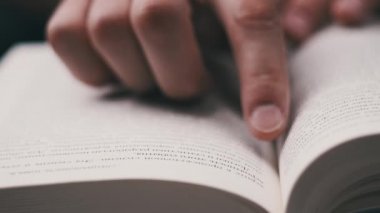Genç adam kitap okuyor ve sayfaları çeviriyor, kapat, yavaş çekim. Erkek el bir kitabı tutar ve öğrenirken parmaklarını sayfa boyunca hareket ettirir. Adam sayfaları karıştırıyor. Metin okumak, öz eğitim
