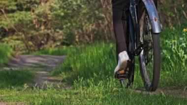 Güneşli bir yaz gününde yeşil orman yolunda bisiklet süren genç bir kadın. Ağır çekim. Bisikletli bir kadın kırsalda yeşil çimlerin çok yakınında patikaya çıkıyor. Sağlıklı bisiklet yaşam tarzı, boş zaman aktivitesi.