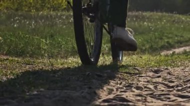 Güneşli bir yaz gününde, yeşil bir alanda bisiklet süren bir kadın orman yolu boyunca bisiklet sürüyor. Ağır çekim. Bisikletli bir kadın kırsal alandaki çayırların çok yakınında geziyor. Boş zaman aktivitesi, sağlıklı bisiklet yaşam tarzı