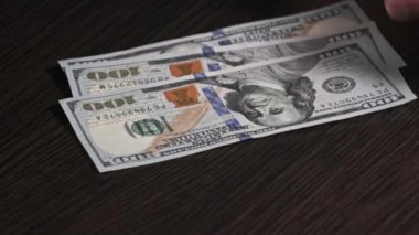 Siyah ahşap bir masadaki yeni yüz dolarlık banknotları sayıyorum. Erkek eller kağıt para sayıyor, ev parası. 100 dolarlık banknotlar sayan bir elin yakın çekimi. İş, finans, ekonomi kavramı.