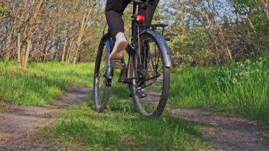 Güneşli bir yaz gününde yeşil bir ormanda bisiklet süren bir kadın. Ağır çekim. Bisikletli bir kadın kırsal alandaki çayırların çok yakınında geziyor. Boş zaman aktivitesi, sağlıklı bisiklet yaşam tarzı