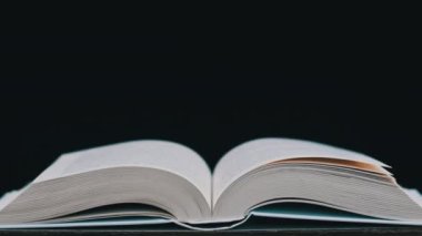 Beyaz kitabın sayfaları rüzgarın etkisiyle rastgele yer değiştiriyor. Kitabın sayfaları yavaş çekimde kendi kendine dönüyor, yakın çekimde. Stüdyoda siyah arka plan üzerine açık bir kitap