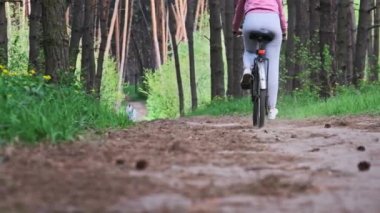 Kırsal bir parkta yeşil ağaçlar arasında bisiklet süren bir kadın. Bisikletli genç bir kadın yaz günü yol boyunca ağır çekimde bisiklet sürüyor. Spor yaşam tarzı, boş zaman aktivitesi, tatil