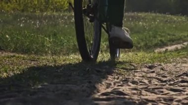 Güneşli bir yaz gününde yeşil orman yolunda bisiklet süren genç bir kadın. Ağır çekim. Bisikletli bir kadın kırsalda yeşil çimlerin çok yakınında patikaya çıkıyor. Sağlıklı bisiklet yaşam tarzı, boş zaman aktivitesi.