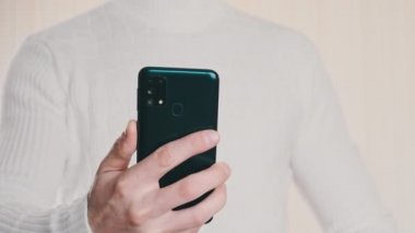 Akıllı telefonu olan genç bir adam soğuk kripto cüzdanındaki QR kodunu tarıyor ve işlem yapıyor. Beyaz arka planda Bitcoin göndermek için modern cihaz kamerası kullanılıyor. Dijital para, güvenli, gelecek konsepti. 4K.