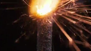 Ağır çekimde siyah arka planda aydınlatma maytap, makro çekim. Barut serpintisinden kıvılcımlar. Havai fişek yangını karanlıkta izole edilmiş. Tatil, yeni yıl konsepti. Yakın çekim havai fişek yanığı.