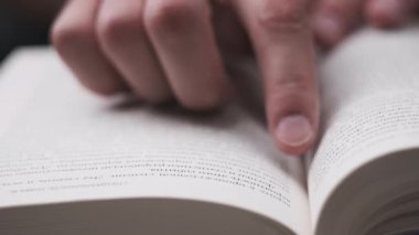 Genç adam kitap okuyor ve sayfaları çeviriyor, kapat, yavaş çekim. Erkek el bir kitabı tutar ve öğrenirken parmaklarını sayfa boyunca hareket ettirir. Adam sayfaları karıştırıyor. Metin okumak, öz eğitim