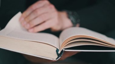 Genç adam kitap okuyor ve sayfaları çeviriyor, kapat, yavaş çekim. Erkek eller bir kitap tutuyor ve sayfaları çeviriyor. Tanımlanamayan bulanık bir adam metni inceliyor. Öğrenme, kendini eğitme. 4K