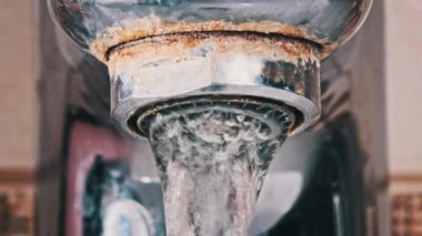 Ağır çekimde akan suyla birlikte makro musluk. Havalandırmadan bir su püskürtüsü, eski bir musluktan banyodaki bir lavaboya akmaktadır. Su açılıp kapanıyor. Yakın plan..