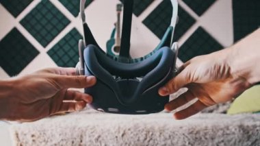 POV of putting on VR glasses virtual reality in the living room. Young male hands hold virtual reality helmet indoors. Virtual reality mask. Close-up. Point of view man taking of VR helmet at home.