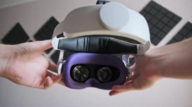 POV of putting on VR glasses virtual reality in the living room. Young male hands hold virtual reality helmet indoors. Virtual reality mask. Close-up. Point of view man taking of VR helmet at home.