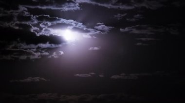 Timelapse of moon moves in the night sky through dark clouds. The mystical moon rises up against the background of clouds. Moonlight shines in the black night sky. Time lapse.