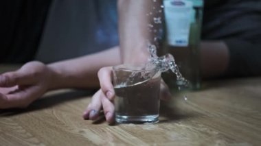 Bir alkolik yere düşer ve yere bir bardak votka dökülmüştür. Aşırı dozda alkol. Alkolizm, sarhoş bir gencin elinin şişenin yanına düşmesi. Yakın plan. Ağır çekim. Alkol bağımlılığı