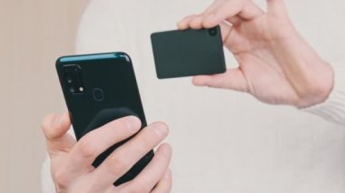 Akıllı telefonu olan genç bir adam soğuk kripto cüzdanındaki QR kodunu tarıyor ve işlem yapıyor. Beyaz arka planda Bitcoin göndermek için modern cihaz kamerası kullanılıyor. Dijital para, güvenli, gelecek konsepti. 4K.