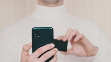 Akıllı telefonu olan genç bir adam soğuk kripto cüzdanındaki QR kodunu tarıyor ve işlem yapıyor. Beyaz arka planda Bitcoin göndermek için modern cihaz kamerası kullanılıyor. Dijital para, güvenli, gelecek konsepti. 4K.