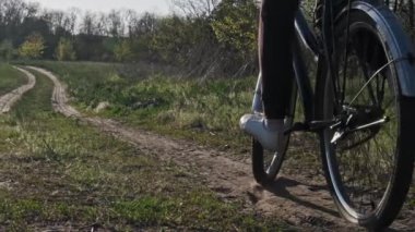 Güneşli bir yaz gününde, yeşil bir alanda bisiklet süren bir kadın orman yolu boyunca bisiklet sürüyor. Ağır çekim. Bisikletli bir kadın kırsal alandaki çayırların çok yakınında geziyor. Boş zaman aktivitesi, sağlıklı bisiklet yaşam tarzı