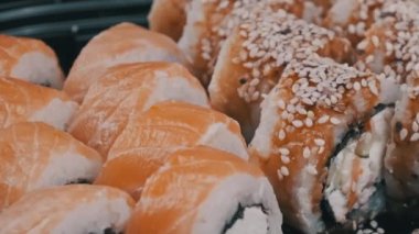 Sushi rolls in plastic box is rotating, close-up. Takeaway fresh Japanese sushi with Philadelphia cheese, nori, sesame, salmon fillets rice, avocado and cucumber. Sushi set in plastic container.