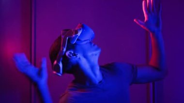 Man in a virtual reality helmet illuminated in red and blue plays a game. Young man in VR headset moves his hands in virtual space. Futuristic technology to play simulation 3D video games Metaverse 4K