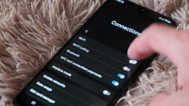 Turning on and off Wi-Fi on a smartphone. The wifi button is turned on the mobile phone in the connections menu. Male finger hand touching touchscreen on modern smart phone with wi fi zone on screen.