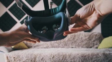Bakış açısına göre genç adam iç mekanda sanal gerçeklik kaskı takıyor. Sanal gerçeklik için sanal gerçeklik gözlüğü takmak. Genç erkek eller sanal gerçeklik kaskını içeride tutuyor. Yakın plan. Oturma odasında VR Maskesi Kullanılıyor