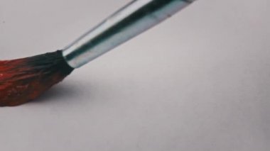 Brush with red paint draws a line on white paper in super macro. Drawing line with red paint, extreme close-up. Painting with watercolor or gouache paint on a white sheet.