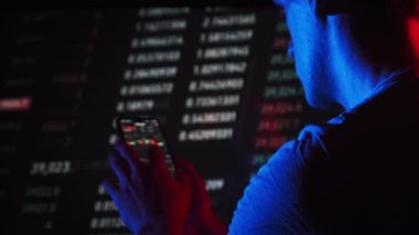Investor checking cryptocurrency price on smartphone screen on exchange backdrop. Many crypto assets change prices. Stock charts of exchange rate. Businessman analyze digital stock market investments