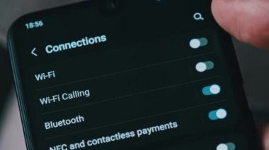 Turning on and off Wi-Fi on a smartphone. The wifi button is turned on the mobile phone in the connections menu. Male finger hand touching touchscreen on modern smart phone with wi fi zone on screen.