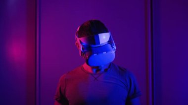Genç adam VR Helmet 'te 360 medya içeriği izliyor. Erkek, kırmızı-mavi ışıkta sanal gerçeklikle sanal gerçeklik arasında bağlantı kurar. Fütürist teknoloji. Meta-evrene dalma, artırılmış gerçeklik, metaevren