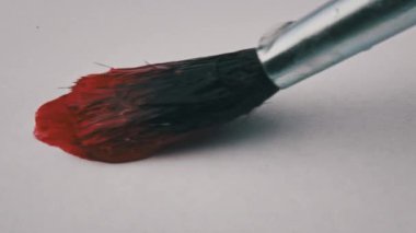 Brush with red paint draws a line on white paper in super macro. Drawing line with red paint, extreme close-up. Painting with watercolor or gouache paint on a white sheet.