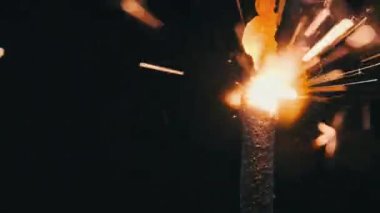 Ağır çekimde siyah arka planda aydınlatma maytap, makro çekim. Barut serpintisinden kıvılcımlar. Havai fişek yangını karanlıkta izole edilmiş. Tatil, yeni yıl konsepti. Yakın çekim havai fişek yanığı.
