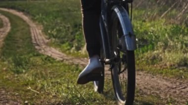 Güneşli bir yaz gününde yeşil orman yolunda bisiklet süren genç bir kadın. Ağır çekim. Bisikletli bir kadın kırsalda yeşil çimlerin çok yakınında patikaya çıkıyor. Sağlıklı bisiklet yaşam tarzı, boş zaman aktivitesi.