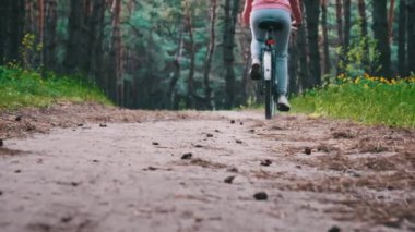 Bisikletli genç bir kadın yaz günü orman yolunda ağır çekimde bisiklet sürüyor. Kırsal bir parkta yeşil ağaçların arasında bisiklet süren bir kadın. Spor yaşam tarzı, boş zaman aktivitesi, tatil