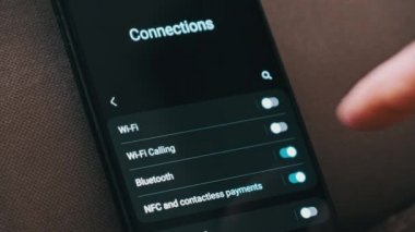 Turning on Wi-Fi on a smartphone. The wifi button is turned on the mobile phone in the connections menu. Male finger hand touching touchscreen on modern smart phone with wi fi zone on screen.