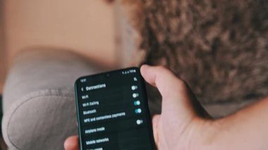 Turning on and off Wi-Fi on a smartphone. The wifi button is turned on the mobile phone in the connections menu. Male finger hand touching touchscreen on modern smart phone with wi fi zone on screen.