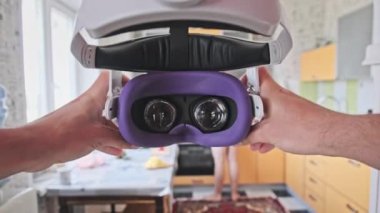 POV man putting on VR helmet at home kitchen. Point of view taking on virtual reality glasses at home. Young male hands hold VR helmet indoors. Immersion in meta-universe, augmented reality, metaverse