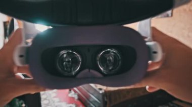 POV of putting on VR glasses virtual reality in the bedroom. Young male hands hold virtual reality helmet indoors. Virtual reality mask. Close-up. Point of view man taking of VR helmet at home.