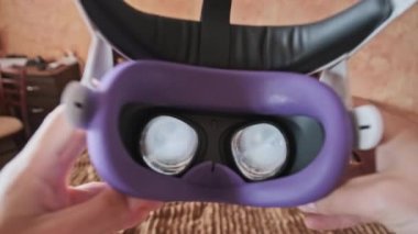 Point of view man taking on VR helmet at bedroom. POV of putting on VR glasses virtual reality at home. Young male hands hold virtual reality helmet indoors. Immersion in the meta-universe, Metaverse