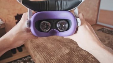 Point of view man taking on VR helmet at bedroom. POV of putting on VR glasses virtual reality at home. Young male hands hold virtual reality helmet indoors. Immersion in the meta-universe, Metaverse