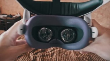 Point of view man taking on VR helmet at bedroom. POV of putting on VR glasses virtual reality at home. Young male hands hold virtual reality helmet indoors. Immersion in the meta-universe, Metaverse