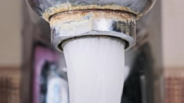 Ağır çekimde akan suyla birlikte makro musluk. Havalandırmadan bir su püskürtüsü, eski bir musluktan banyodaki bir lavaboya akmaktadır. Su açılıp kapanıyor. Yakın plan..