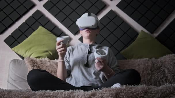 Ung Kvinne Virtuell Virkelighetshjelm Som Sitter Sofa Flytter Styrespaker Hendene – stockvideo