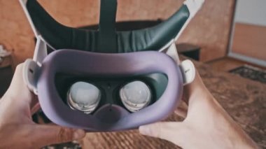 POV of putting on VR glasses virtual reality in the bedroom. Young male hands hold virtual reality helmet indoors. Virtual reality mask. Close-up. Point of view man taking of VR helmet at home.
