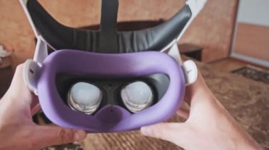 Point of view man taking on VR helmet at bedroom. POV of putting on VR glasses virtual reality at home. Young male hands hold virtual reality helmet indoors. Immersion in the meta-universe, Metaverse