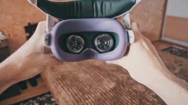 Point of view man taking on VR helmet at bedroom. POV of putting on VR glasses virtual reality at home. Young male hands hold virtual reality helmet indoors. Immersion in the meta-universe, Metaverse