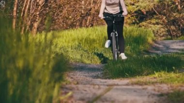 Güneşli bir yaz gününde yeşil bir ormanda bisiklet süren bir kadın. Ağır çekim. Bisikletli bir kadın kırsal alandaki çayırların çok yakınında geziyor. Boş zaman aktivitesi, sağlıklı bisiklet yaşam tarzı